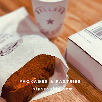 Chocolate loaf pastry in white packaging beside a pink cup and a bakery box on a wooden table
