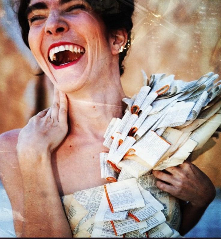 Smiling person in a white dress covered with banknotes, laughing outdoors.