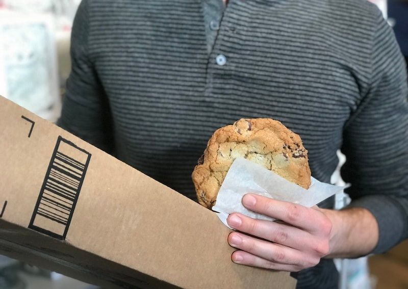 Person holding a muffin and an Amazon shipping box indoors