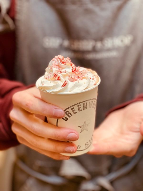 Hands holding a cup of whipped cream-topped dessert in a branded paper cup