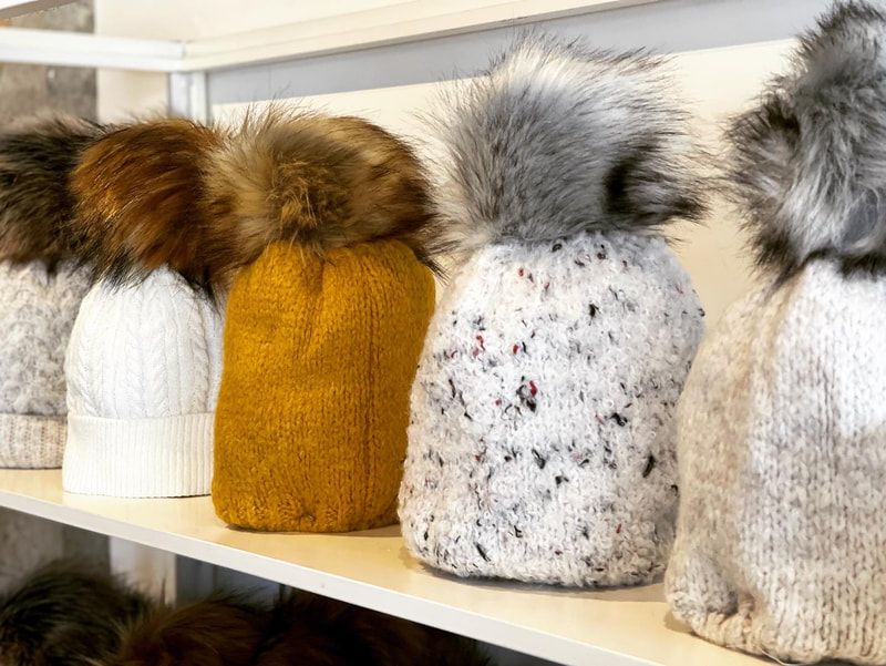 Furry winter hats in white, mustard, gray, and beige on a shelf