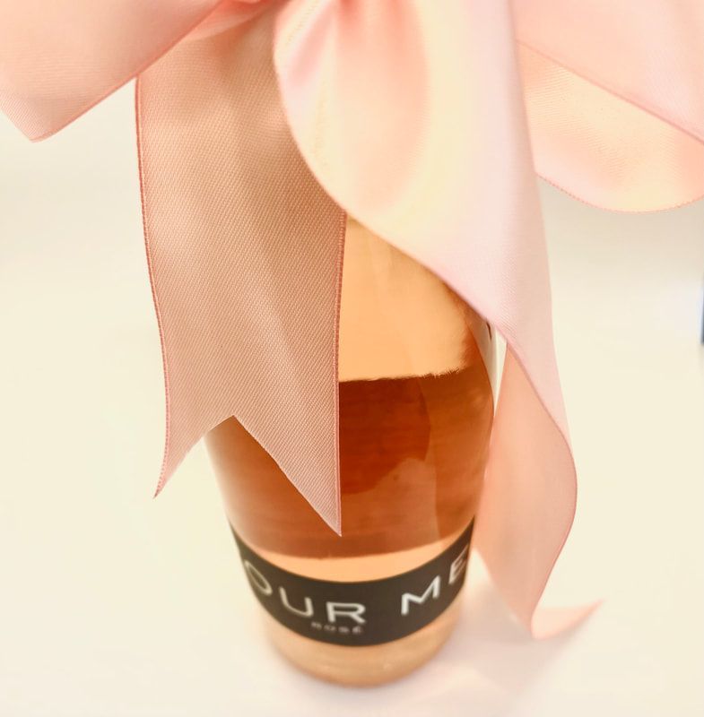 Pink flower petals surrounding a rose-gold perfume bottle with a black label