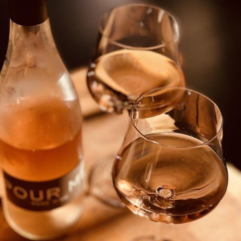 Two glasses of amber liquor beside a frosted bottle on a warm wooden table
