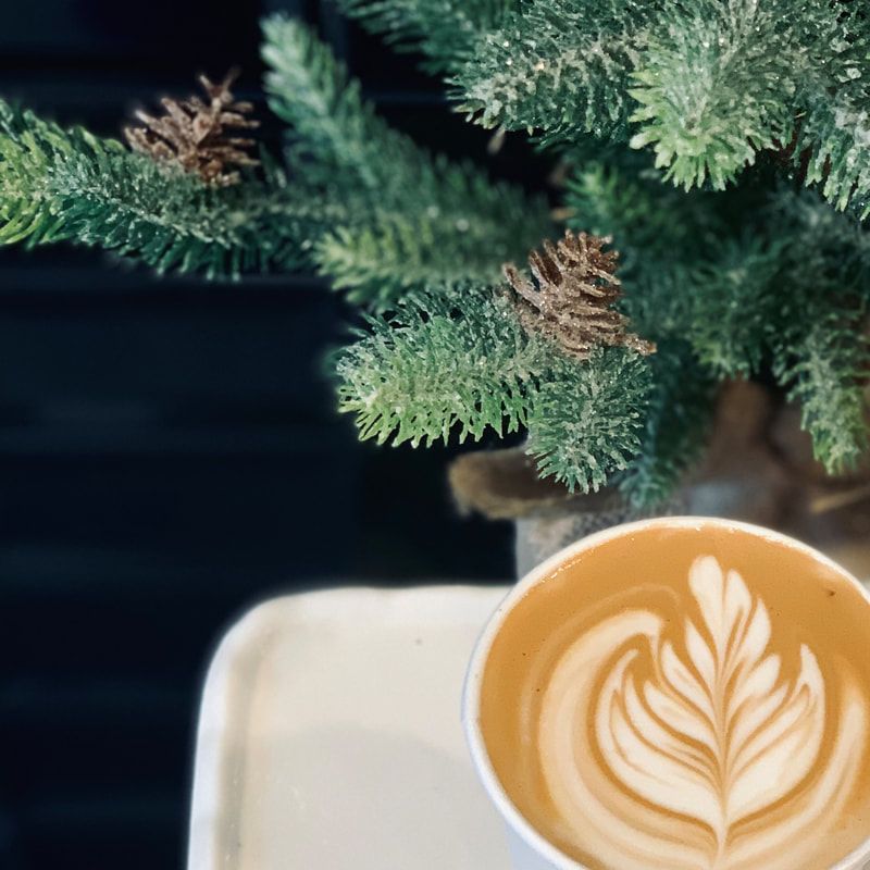 Latte with leaf latte art beside a small evergreen branch on a white table