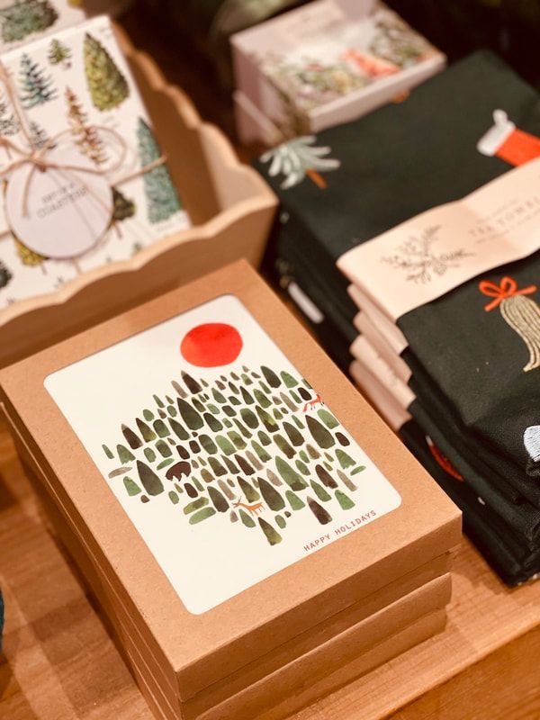 Stacked gift boxes with a square card showing a red sun over green trees