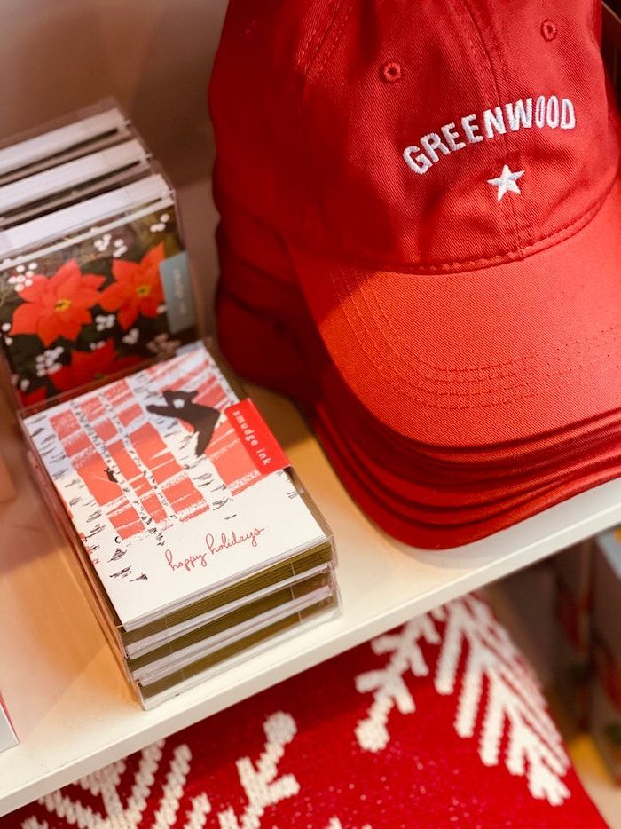 Red Greenwood cap on a shelf beside stacks of cards and a red snowflake blanket