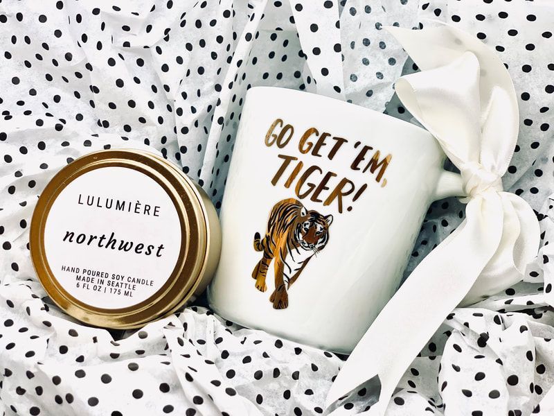 White mug reading “Go get ’em tiger!” beside a round “northwest” candle on black-and-white polka dot fabric.