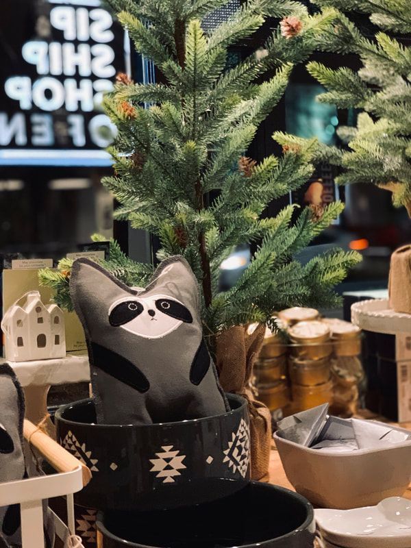 Potted faux evergreen with a raccoon figurine in a black planter on a store shelf