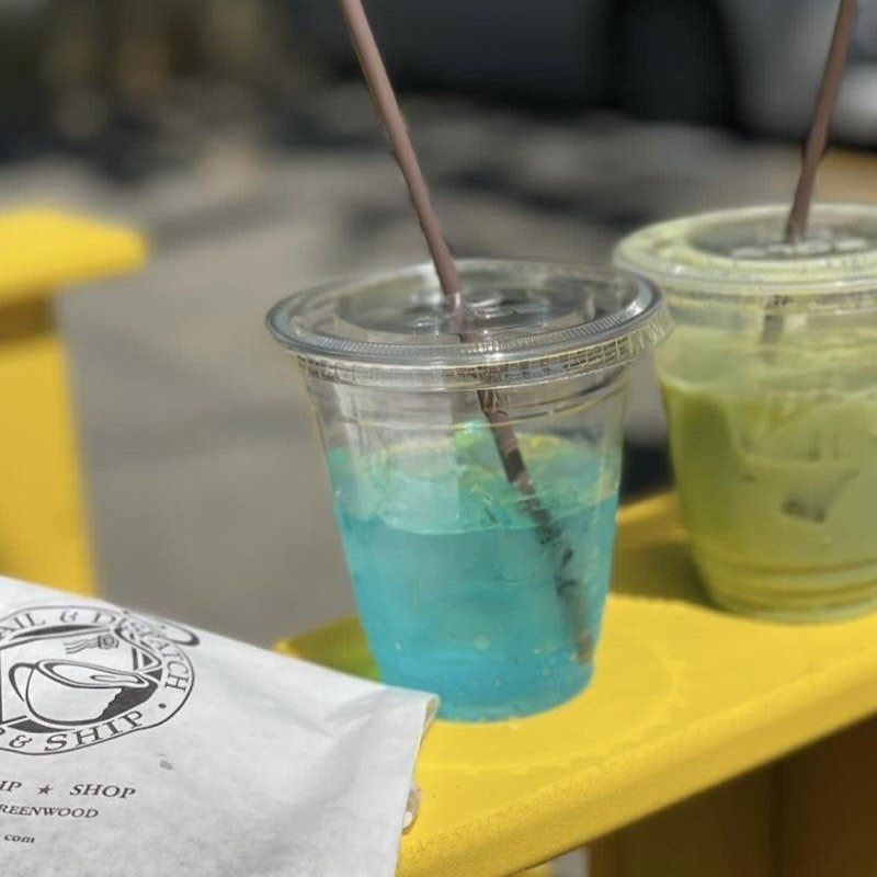 Two iced drinks in clear cups on a yellow table, one blue and one green, with straws.