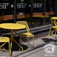 Yellow café tables and chairs outside a storefront with “SIP SHOP” signage