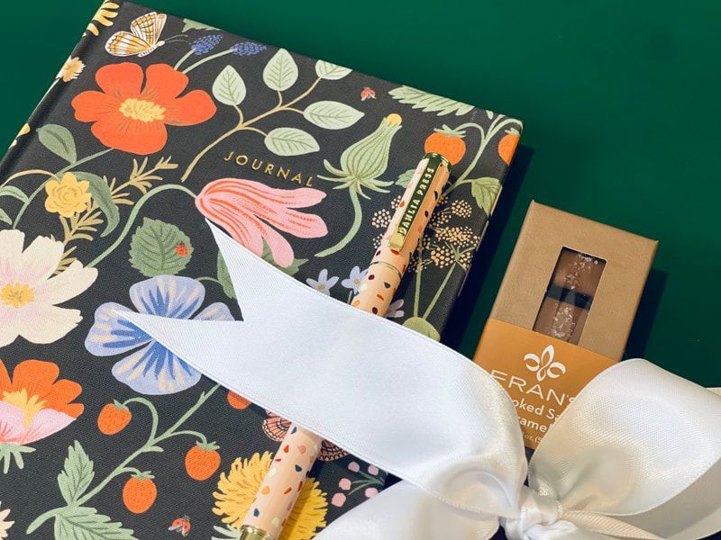 Gift set with floral notebook, pen, and ribbon-tied package on a green background