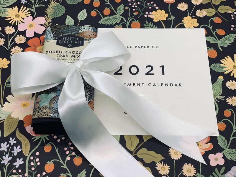 White ribbon bow on a 2021 calendar over a dark floral-patterned background