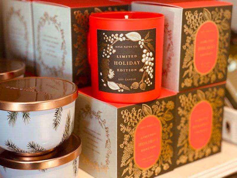 Holiday candles in red and gold packaging, with decorative tins on display.