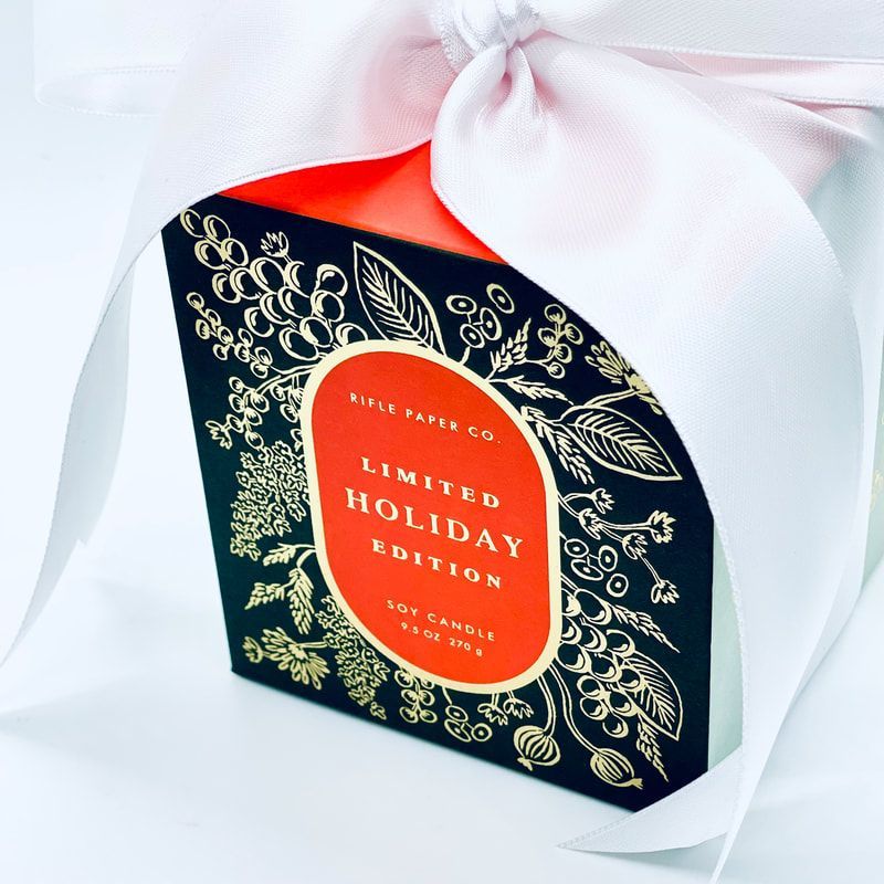 Limited holiday edition gift box with navy, gold, and red design, tied with a pink ribbon