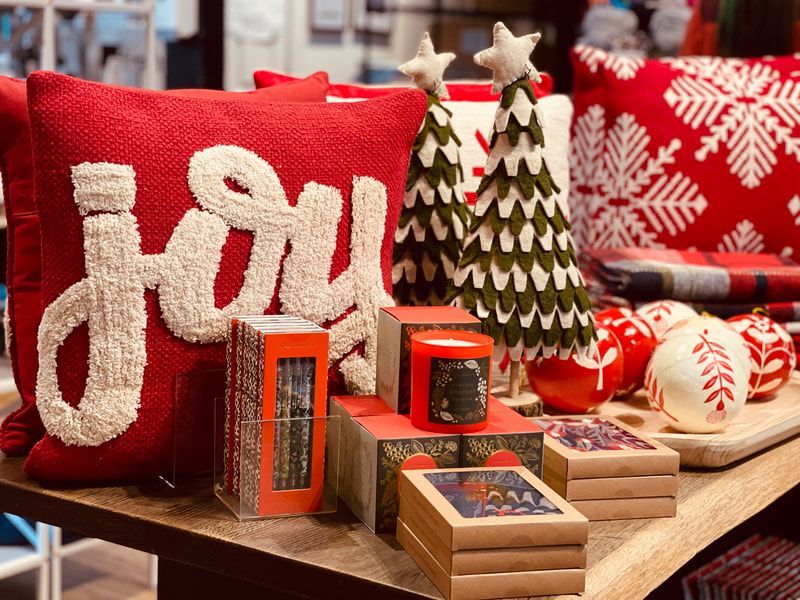 Holiday gift display with red pillows, festive ornaments, and small wrapped boxes on a wooden table