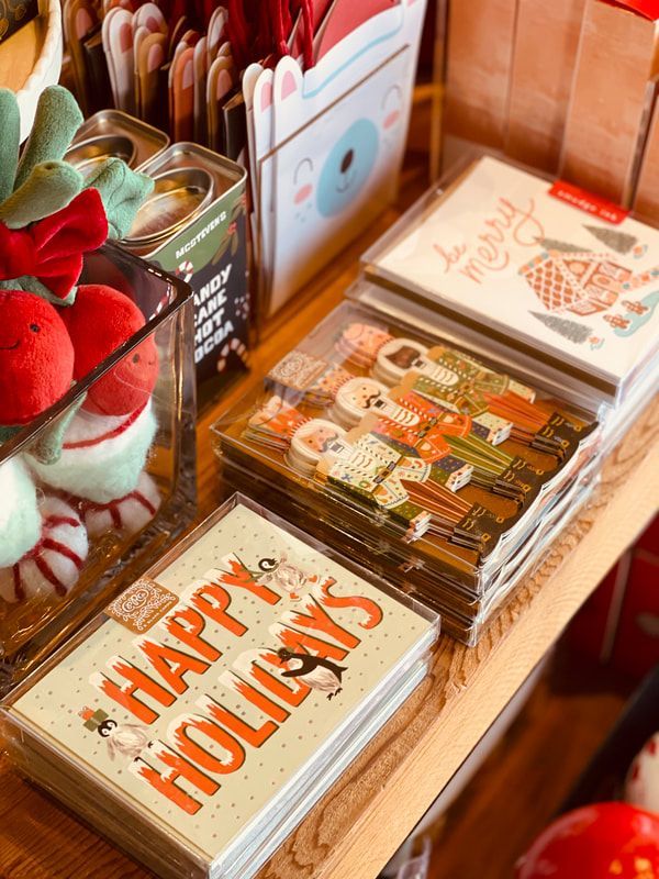 Holiday greeting cards displayed on a woven mat, including a “Happy Holidays” card and festive red decorations