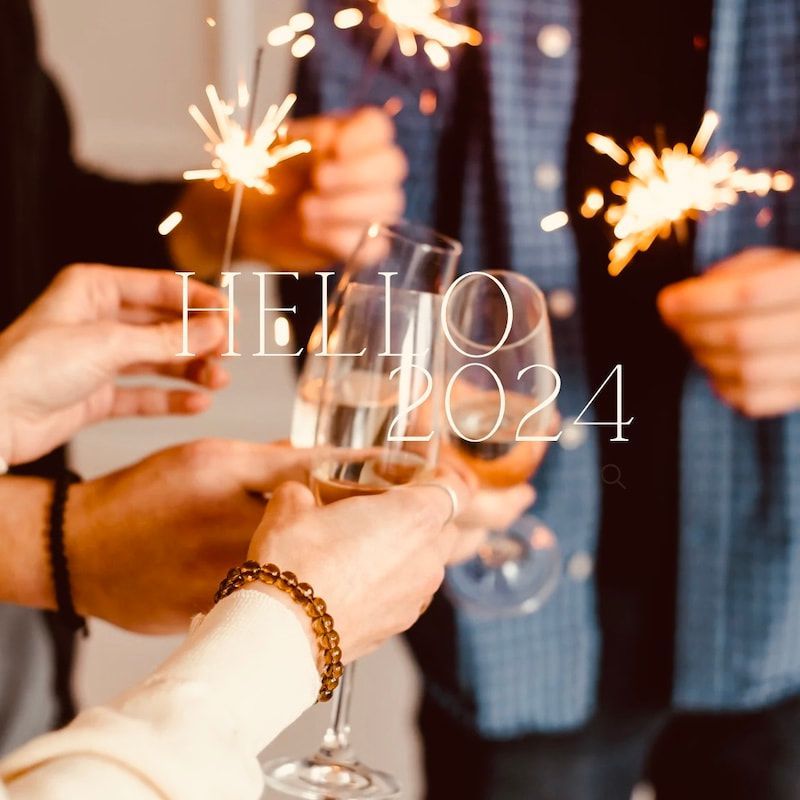 Hands raising champagne flutes at a warm holiday party with sparklers and “HELLO 2024” text