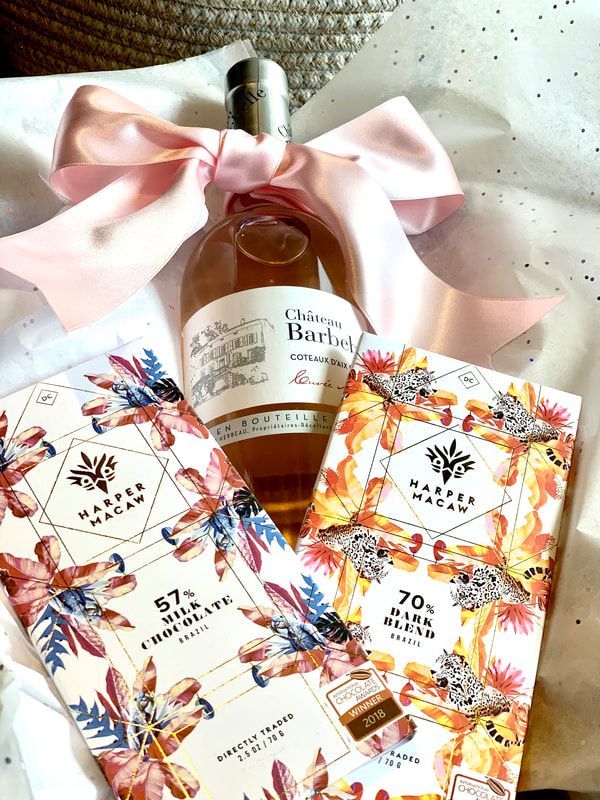 Gift set with pink ribbon, rose bottle, and floral cards on a white textured background
