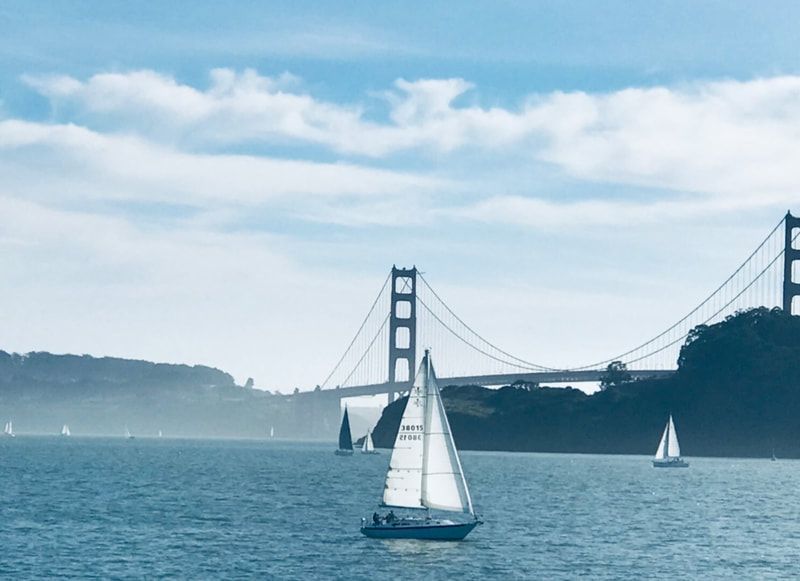 Sailboat on blue water with the Golden Gate Bridge and foggy hills in the background