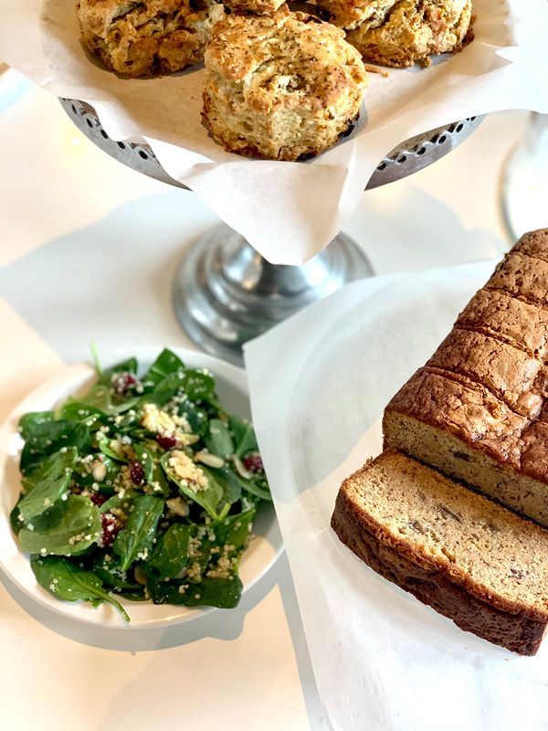 Pastries on a silver stand with a salad bowl and sliced bread on a white table