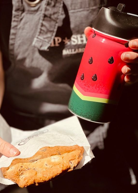 Hand holding a watermelon-themed tumbler and a pastry on napkins outdoors