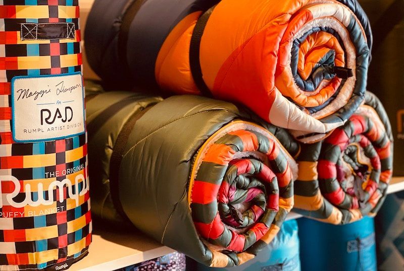 Rolled colorful woven blankets stacked on a shelf in a market stall.