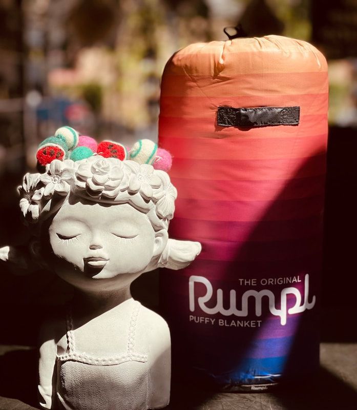White doll bust with colorful hair beside a pink-to-blue Rumpl blanket sack