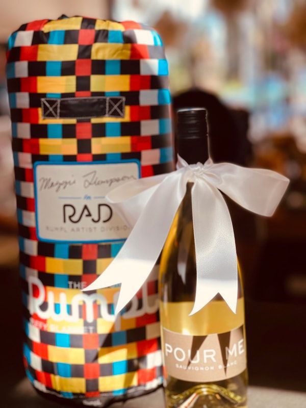 Colorful woven gift basket with a white bow and a bottle of wine beside it