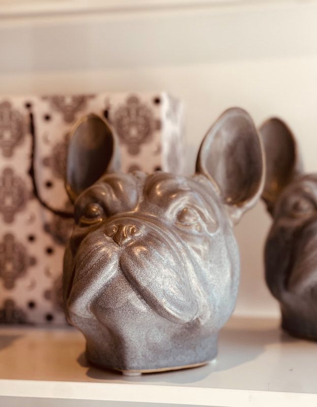 Bronze bulldog figurine with large ears on a shelf, with patterned decor in the background