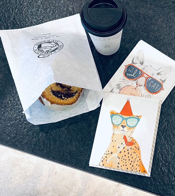 Coffee cup and three cat-themed cards on a table, one holding a pastry in a paper bag