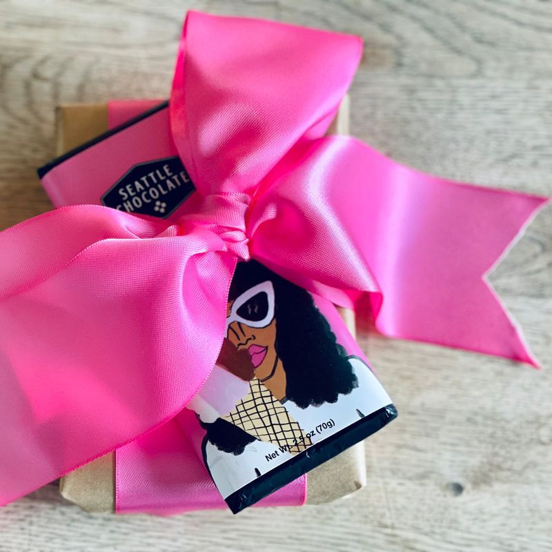 Gift box tied with a bright pink ribbon, featuring a Seattle Chocolate bar on top.