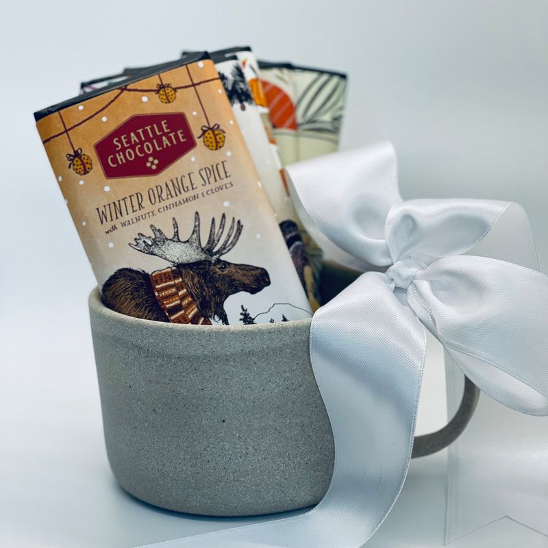Gift basket with a white ribbon, chocolate mix, and a mug in a gray cup-shaped holder.