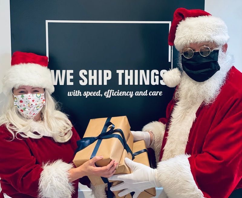 Santa-clad shipping staff hold a wrapped package in front of a “WE SHIP THINGS” sign.
