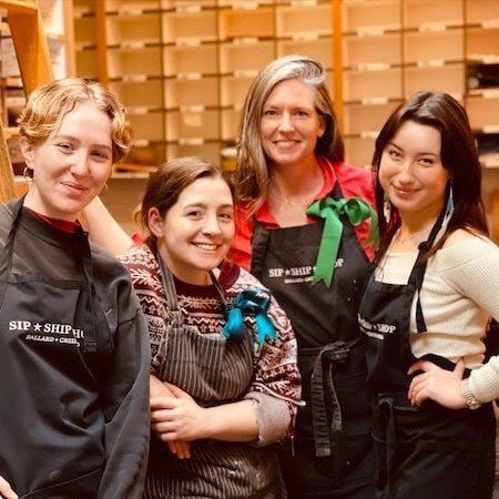 Four people in aprons smiling together in a warm indoor kitchen setting