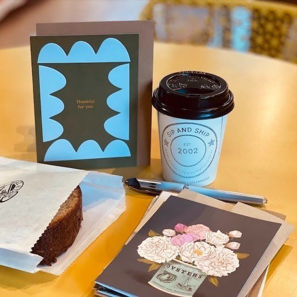 Gift items on a table: framed card, candle, cake slice, pen, and floral card.