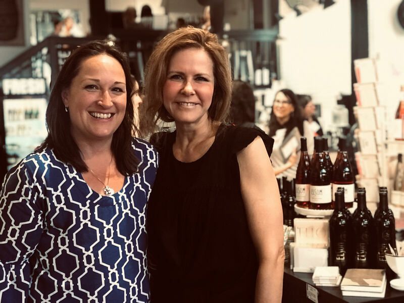 Two women smiling beside a display of bottles and jars in a shop