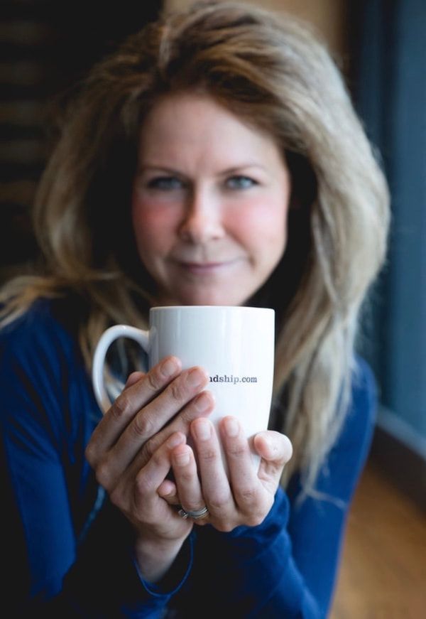 Woman holding a white mug toward the camera in a softly lit indoor setting