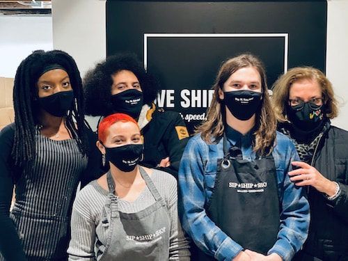 Five masked people posing indoors in front of a SHI sign, one giving a thumbs-up.