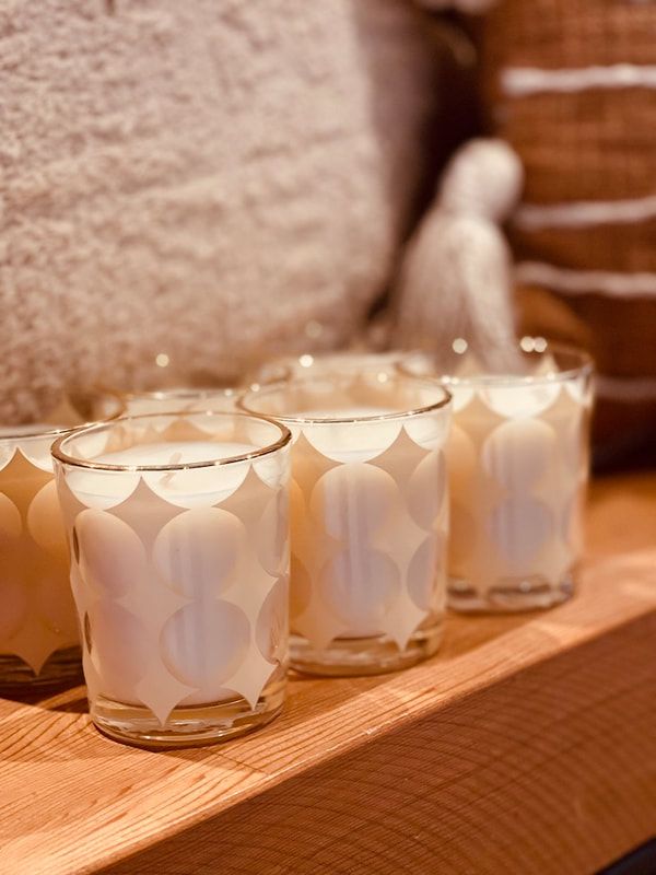 Three small white votive candles on a wooden shelf beside a plush beige chair