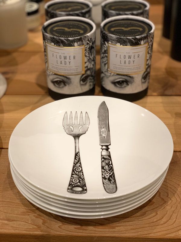 Stack of white plates with ornate silver fork and knife on top, in front of candles on a wooden table