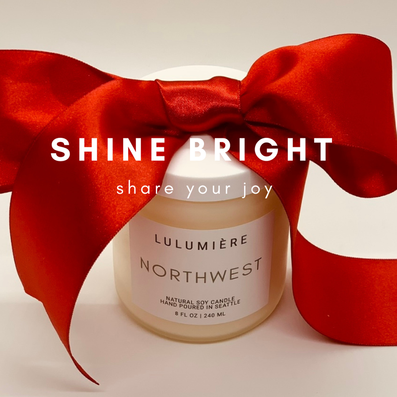 Candle jar with a large red bow and white text reading “SHINE BRIGHT” and “share your joy”