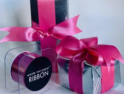 Pink ribbon bows on black and silver gift boxes with a white paper ribbon spool.