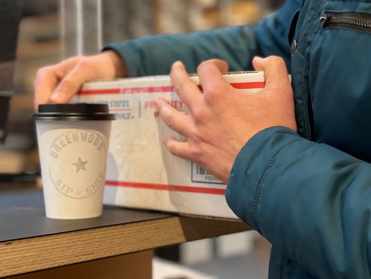Hands holding a cardboard box beside a takeaway coffee cup on a counter