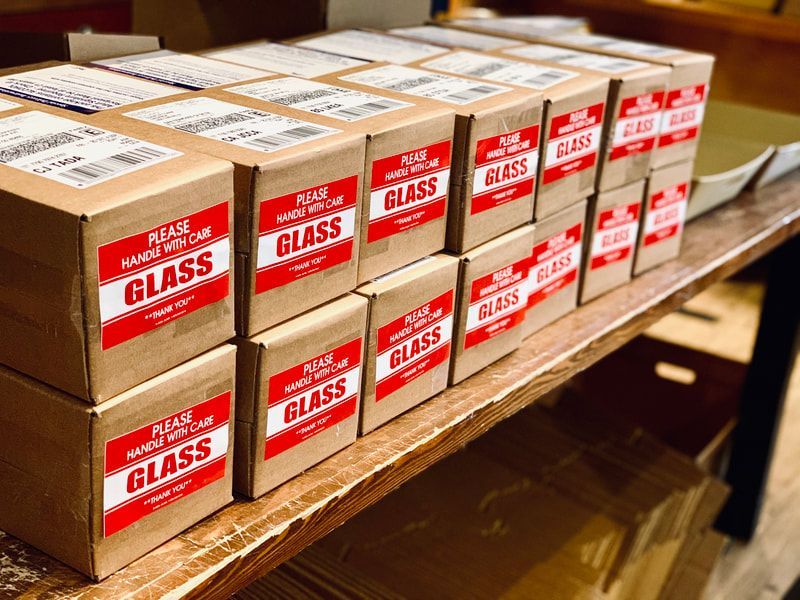 Stacks of cardboard boxes labeled “glass” on a wooden shelf in a warehouse.