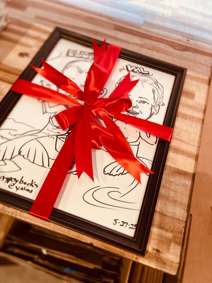 Framed signed sketch tied with a bright red ribbon and bow on a wooden surface