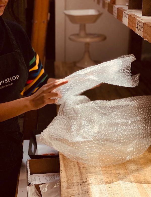 Person packing bubble wrap at a wooden counter in a shop or workshop