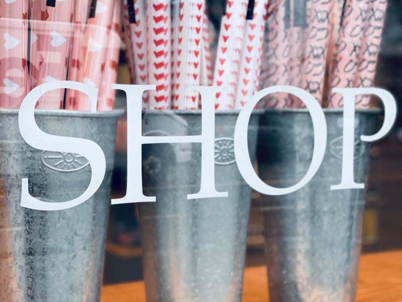 Large white “SHOP” sign in front of hanging pink and gray patterned items