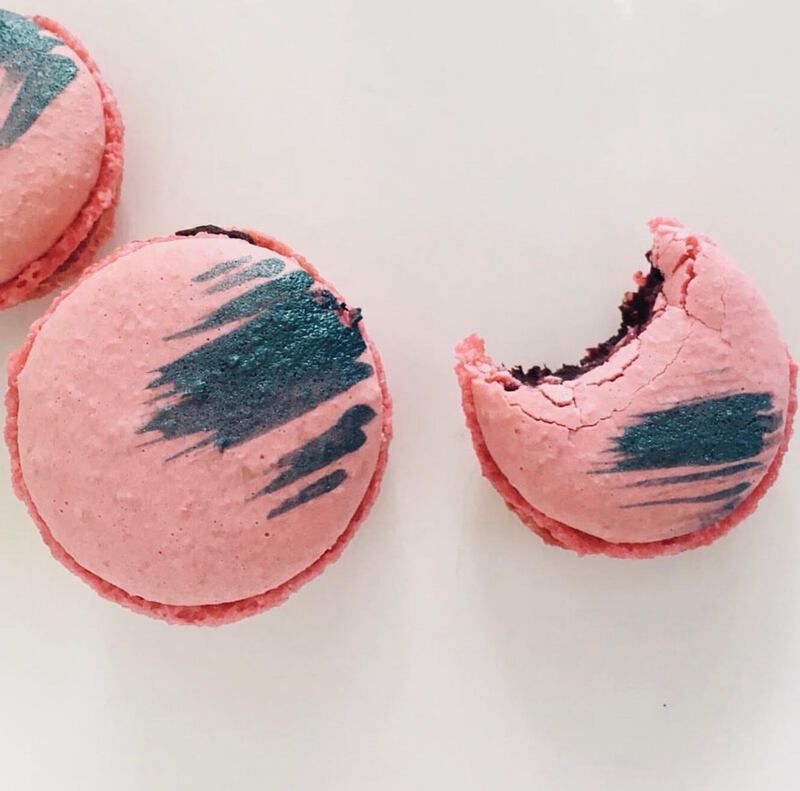 Three pink macarons with teal brushstroke decorations, one broken open on a white background