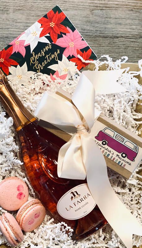 Gift basket with a white ribbon, decorative paper, amber bottle, macarons, and shredded filler on a wooden surface