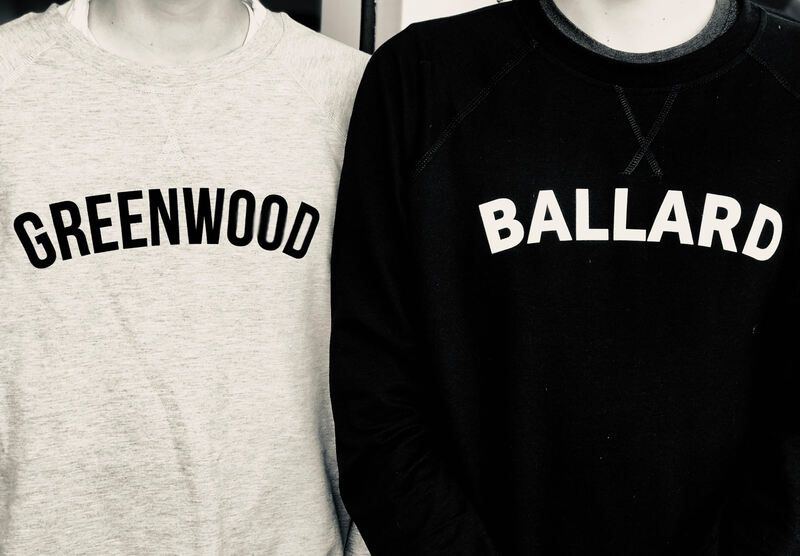 Two people wearing sweatshirts labeled GREENWOOD and BALLARD, one light gray and one black.